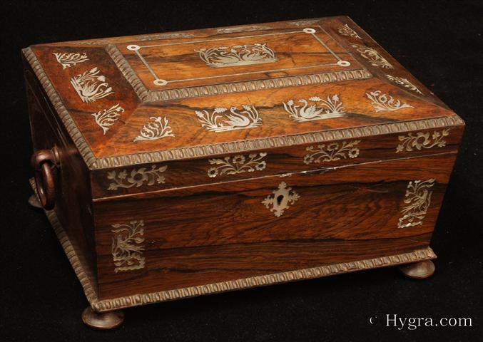 -Antique box in the sarcophagus form. The box is veneered in figured rosewood and is inlaid in mother of pearl depicting stylized flora with birds. The fluid design of stylised flora is exceptionally fine. This is a spectacular box which encapsulates the best of the Regency era. The box stands on turned rosewood feet and has turned rosewood drop ring handles. The centre panel of the top is framed with gadrooning as is the pediment adding the architectural impact. The box has a lift out tray which has been relined . Circa1825. -Enlarge Picture